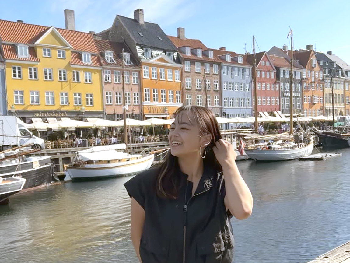 A college student poses for a picture in front of colorful houses and water in Copenhagen